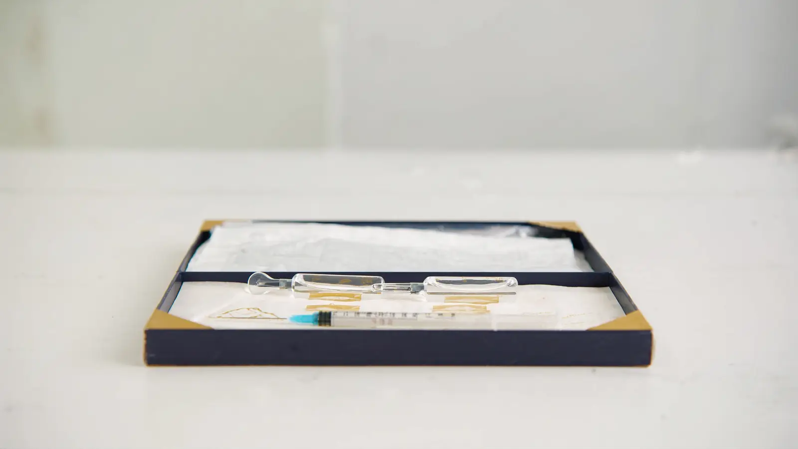 Realistic photographic close-up of a set of sterile skin booster injection vials and a fine needle on a clean navy tray, prem